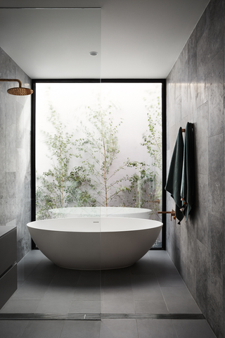 freestanding white bath in a grey stone bathroom with a garden window
