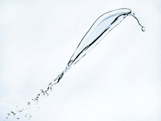 a clear stream of liquid splashing mid-air against a pale blue background