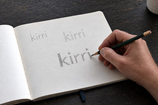 pencil sketches of the kirri wordmark in an open notebook, the dot raised on the final i