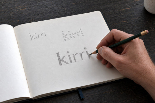 pencil sketches of the kirri wordmark in an open notebook, the dot raised on the final i